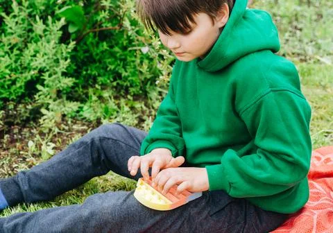 Boy with rainbow Pop It Fidget in hands. Teen in green Playing, Push bubble o Stock Photos