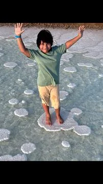 Boy raises arms joyfully while standing barefoot on salt formations, surrounded Stock Photos