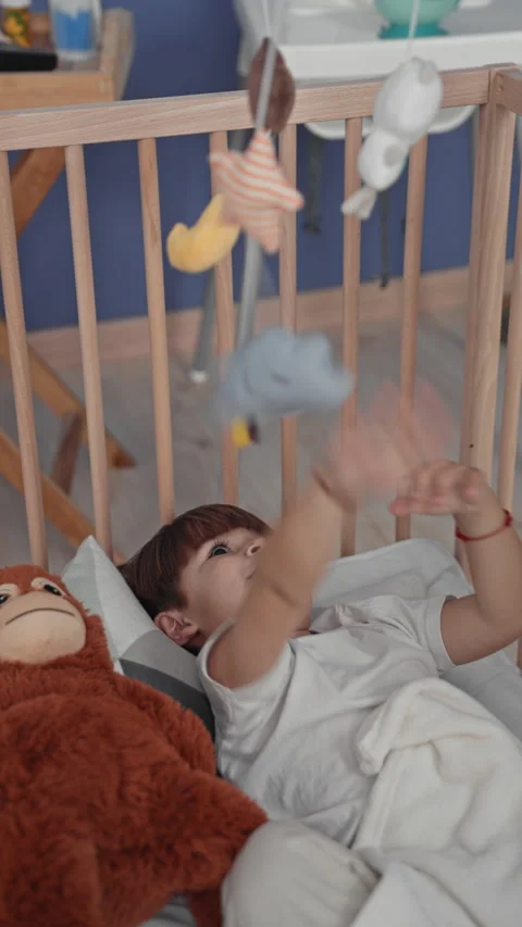 Boy reaching with hand toward hanging crib mobile in a building room, lying.. Stock Footage 339249144