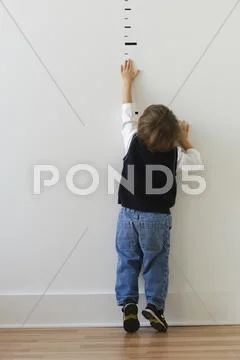 Boy reaching for height markers on wall Stock Photos