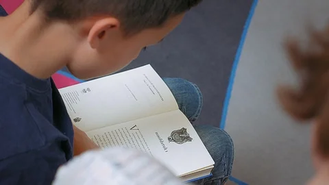 Boy reading aloud sitting next to an adult person Stockbeeldmateriaal 93445094