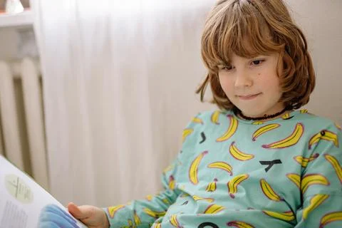 Boy reading a book in bedroom while wearing pajamas with banana print Stock-Fotos