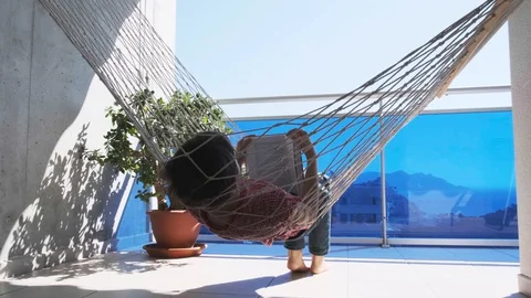 Boy reading book in hammock on balcony. Education, online distance learning Stock-Footage 128942142