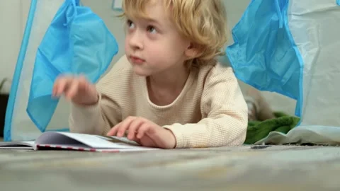 Boy reading a book lying on the floor in the playroom Video stock 303074079