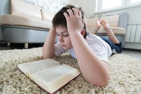 Boy reading a book while lying on  carpet in the room Stock Photos