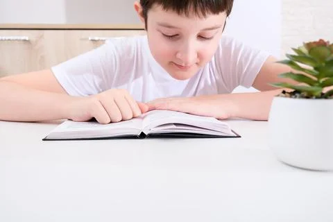 A boy reading a book while sitting by the table Stock Photos