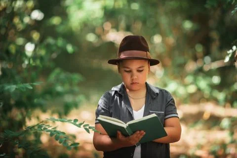 Boy reading an open book in a green forest Foto stock