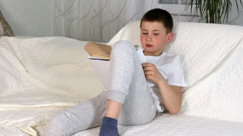 Boy reading paper book aloud, turning pages, studying at home Stock Footage 154309119
