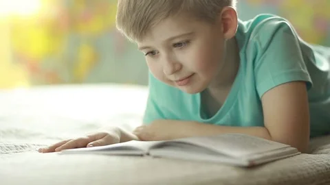  A boy reads a book while lying on a bed. Stock Footage 72870305