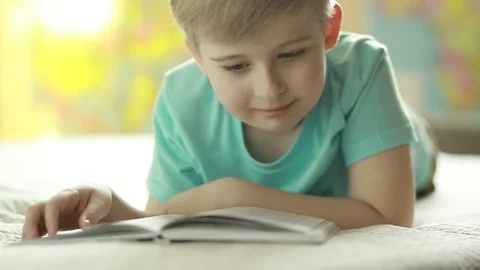  A boy reads a book while lying on a bed. Stock Footage 72870333