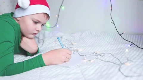 A boy in a red cap of Santa Claus and writes a letter to Christmas Stock Footage 165384000