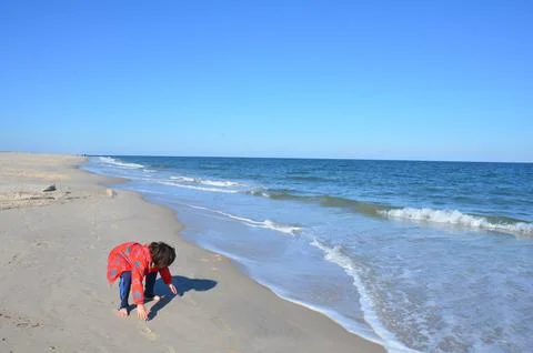 Boy in red jacket and beach with water and sand Stock Photos