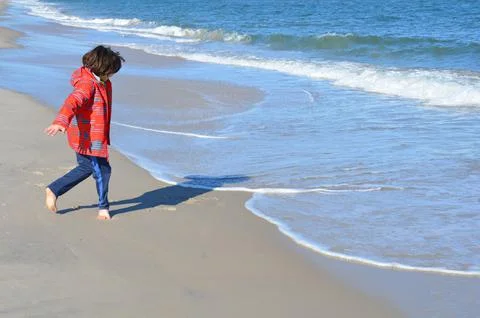 Boy in red jacket and beach with water and sand Stock Photos