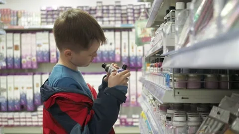 A boy in a red jacket picks out paint on the counter. we look at the jars with Stock Footage 154895669
