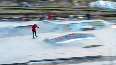 Boy in red jacket practicing tricks in skate part in motion blur Foto stock