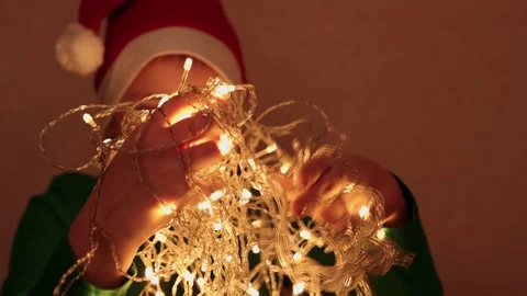 A boy in a red night cap plays with a garland with yellow lights close-up. Stock Footage 165327945