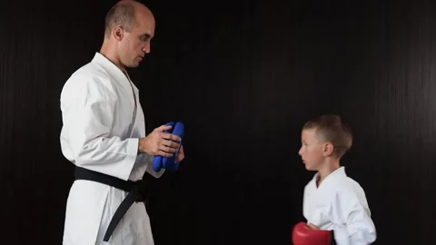 Boy in red pads hits straight punches with his hand on a blue exercise machine Stock Footage 303434033