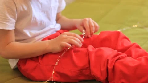 A boy in red pants is sorting through a Christmas garland in his hands Stock Footage 166292356