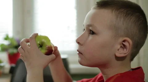 The boy in the red shirt is chewing an apple and looking ahead. Stock Footage 63022791