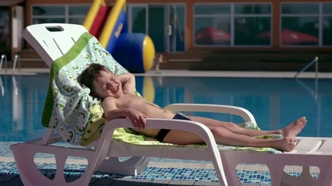 Boy resting and taiking sunbathe on a lounger in the aquapark near the pool Stock Footage 80768337