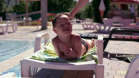 Boy resting and taiking sunbathe on a lounger in the aquapark near the pool Stock Footage 80769010