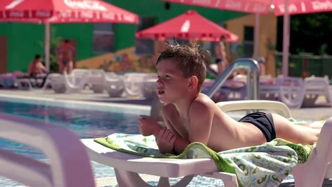 Boy resting and taiking sunbathe on a lounger in the aquapark near the pool Stock Footage 80769427