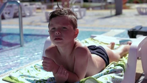 Boy resting and taiking sunbathe on a lounger in the aquapark near the pool Stock Footage 80769760