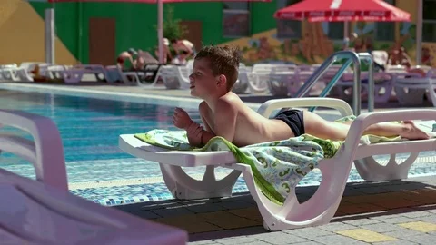 Boy resting and taiking sunbathe on a lounger in the aquapark near the pool Stock Footage 80770770