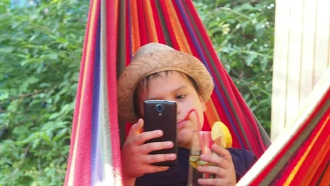 Boy resting in a hammock, drinking a cocktail with lemon, talking on the phone 動画素材 167354877