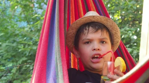 Boy resting in a hammock, drinking a cocktail with lemon, talking on the phone 動画素材 167354889