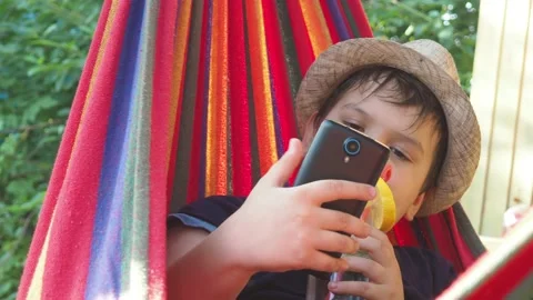 Boy resting in a hammock, drinking a cocktail with lemon, talking on the phone 動画素材 167354906
