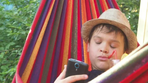 Boy resting in a hammock, drinking a cocktail with lemon, talking on the phone 動画素材 167354918