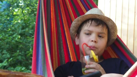 Boy resting in a hammock, drinking a cocktail with lemon, talking on the phone 動画素材 167354940