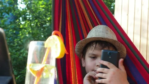 Boy resting in a hammock, drinking a cocktail with lemon, talking on the phone 動画素材 167354948