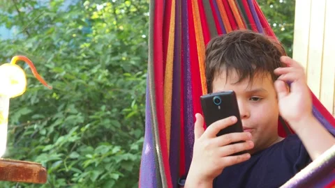 Boy resting in a hammock, drinking a cocktail with lemon, talking on the phone Stock Footage 167354950