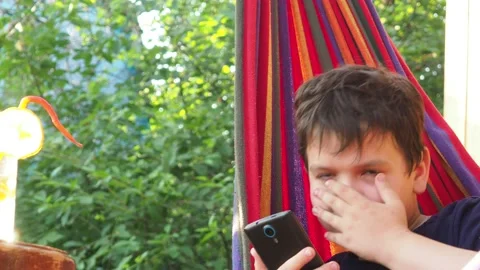 Boy resting in a hammock, drinking a cocktail with lemon, talking on the phone 動画素材 167354952