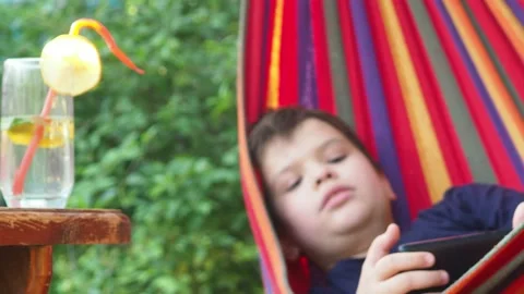Boy resting in a hammock, drinking a cocktail with lemon, talking on the phone 動画素材 167354968