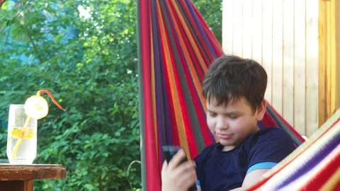 Boy resting in a hammock, drinking a cocktail with lemon, talking on the phone 動画素材 167354976