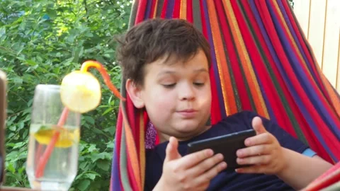 Boy resting in a hammock, drinking a cocktail with lemon, talking on the phone 動画素材 167354980