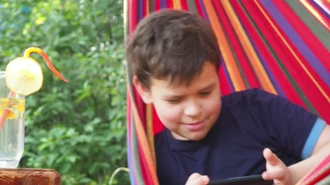 Boy resting in a hammock, drinking a cocktail with lemon, talking on the phone 動画素材 167354993