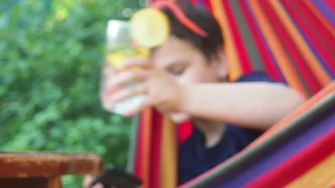 Boy resting in a hammock, drinking a cocktail with lemon, talking on the phone 動画素材 167355005