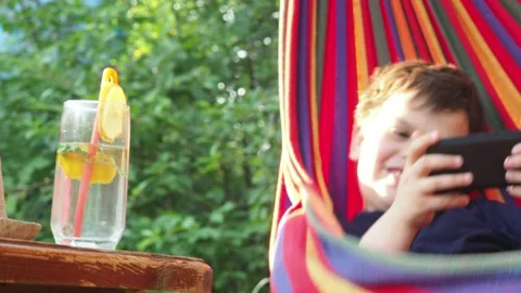 Boy resting in a hammock, drinking a cocktail with lemon, talking on the phone 動画素材 167355009