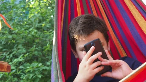 Boy resting in a hammock, drinking a cocktail with lemon, talking on the phone 動画素材 167355011