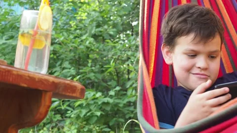 Boy resting in a hammock, drinking a cocktail with lemon, talking on the phone 動画素材 167355025