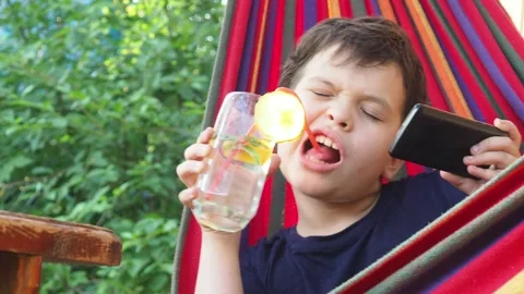 Boy resting in a hammock, drinking a cocktail with lemon, talking on the phone 動画素材 167355031