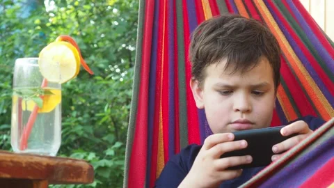 Boy resting in a hammock, drinking a cocktail with lemon, talking on the phone 動画素材 167355033