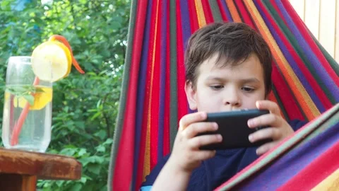 Boy resting in a hammock, drinking a cocktail with lemon, talking on the phone 動画素材 167355038