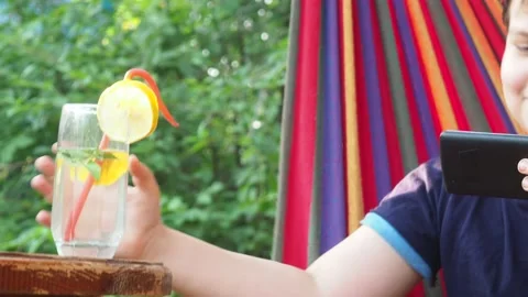 Boy resting in a hammock, drinking a cocktail with lemon, talking on the phone 動画素材 167355083