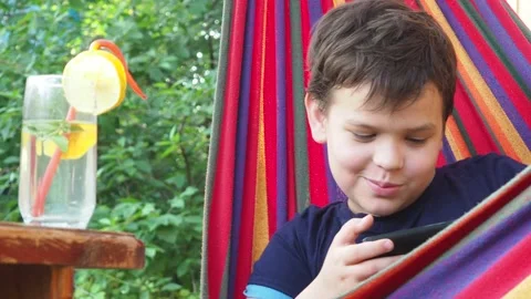 Boy resting in a hammock, drinking a cocktail with lemon, talking on the phone 動画素材 167355084