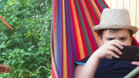Boy resting in a hammock, drinking a cocktail with lemon, talking on the phone 動画素材 167355092